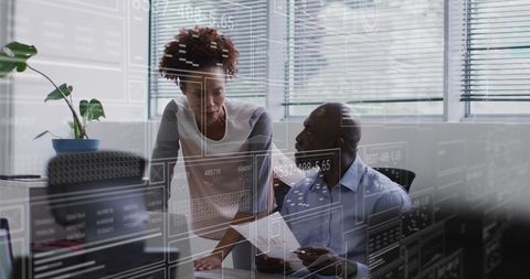 Colleagues collaborating over analytics dashboards at modern office workstation with blinds and dayl