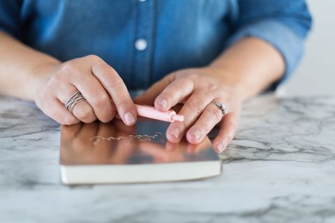 Person's hands holding pen over journal on marble table