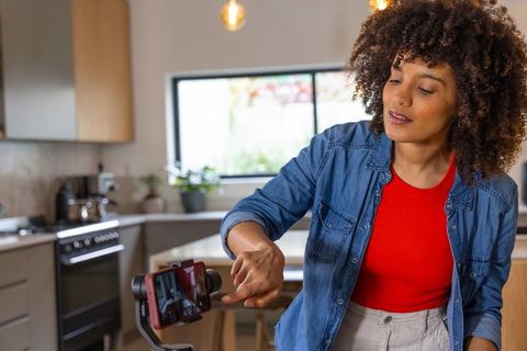 African american woman filming cooking vlog on smartphone gimbal in modern kitchen