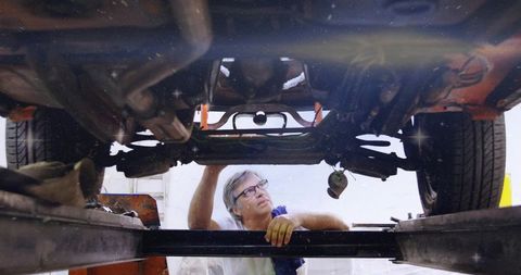 Automotive mechanic inspecting undercarriage on car lift wearing yellow gloves and goggles