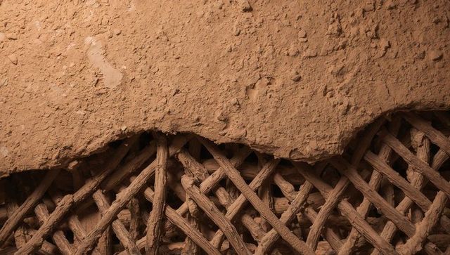 Revealing woven wooden lattice and eroding clay plaster on earthen wall texture
