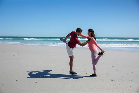 Couple enjoying beach exercise performing stretching routine