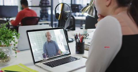 Professional Woman Attending Virtual Meeting on Laptop in Open-Plan Office with Desk Plant