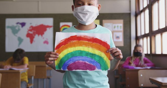 Happy asian boy standing in facemask and showing rainbow picture. School, learning, childhood, health, hygiene, coronavirus, education, unaltered.