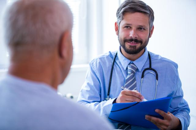 Doctor consulting senior patient in hospital. Doctor holding clipboard and smiling while listening to patient. Ideal for healthcare, medical advice, patient care, and hospital-related content.