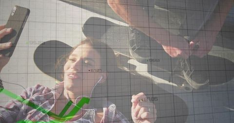 Young woman lying on urban plaza taking selfie with skateboards and financial data overlay