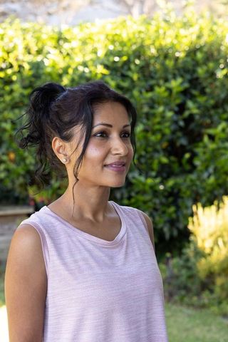 Indian woman standing in backyard garden wearing sleeveless pink knit top and stud earrings