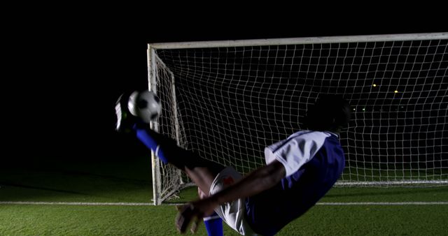Soccer player executing an impressive bicicleta kick in front of goal under stadium lights at night, showcasing agility and athleticism. Perfect for sports blogs, football advertisements, training programs, and inspiration for athletes.