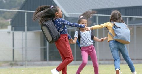 Three Happy Young Schoolgirls Holding Hands and Spinning in School Yard