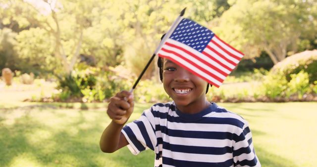 Slow motion portrait of happy boy waving American Flag at park