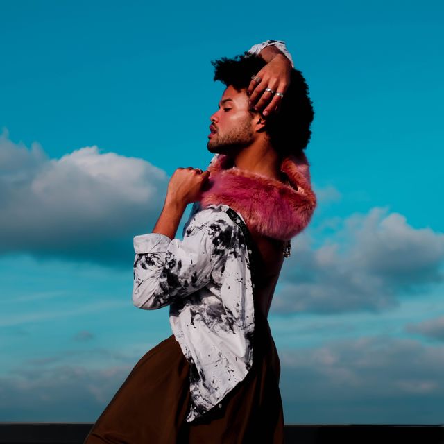 Fashion model striking a confident pose with background of blue sky and clouds. Ideal for fashion magazines, style blogs, advertisement campaigns, and visual arts projects conveying confidence and modern fashion trends.