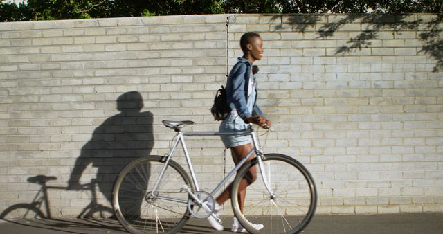 Young Person Walking Bicycle Along Brick Wall on Sunny Day - Download Free Stock Images Pikwizard.com