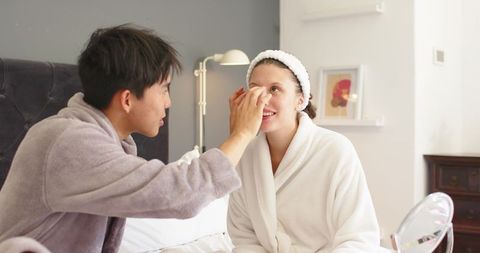 Couple applying skincare in bathrobes on bed during cozy morning self-care routine together
