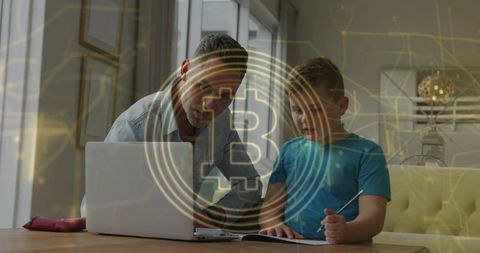 Father teaching son Bitcoin basics using laptop and notebook, home finance learning moment