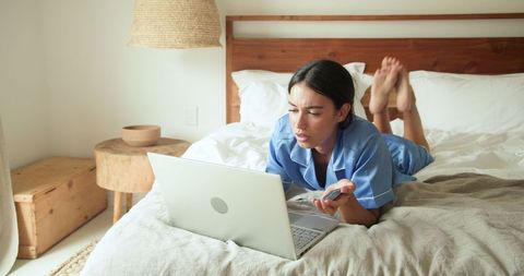 Woman in Blue Pajamas Working Remotely on Cozy Bed Setup