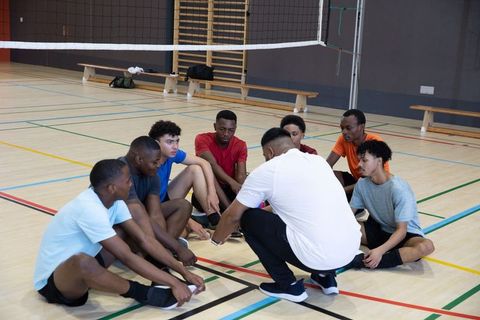 Coach leading african american male athletes in team huddle on indoor volleyball court