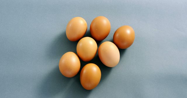 Seven brown eggs arranged on light blue background. Ideal for use in cooking blogs, food packaging, nutritional articles, recipes, promoting organic or farm-fresh produce, and egg-related marketing materials.
