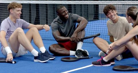 Diverse Friends Chatting on Paddle Tennis Court Holding Rackets