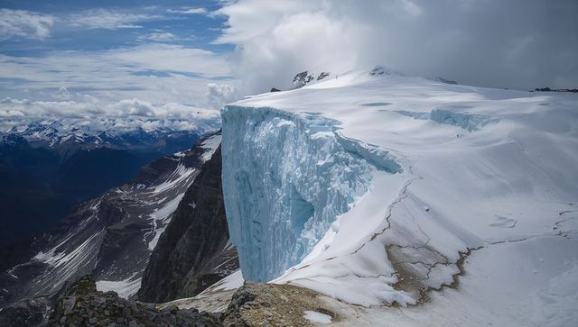 Dominating hanging glacier cliff dropping from snowy plateau on alpine ridge, crevasse detail