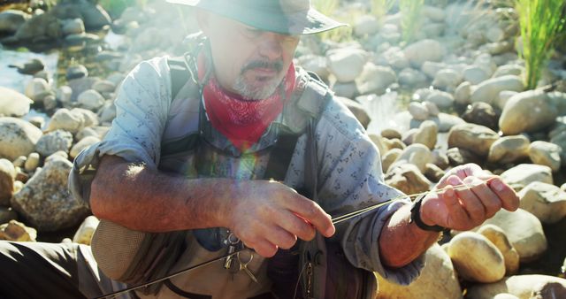 Middle-aged fisherman wearing hat tying fishing line in rocky riverbed - Download Free Stock Images Pikwizard.com