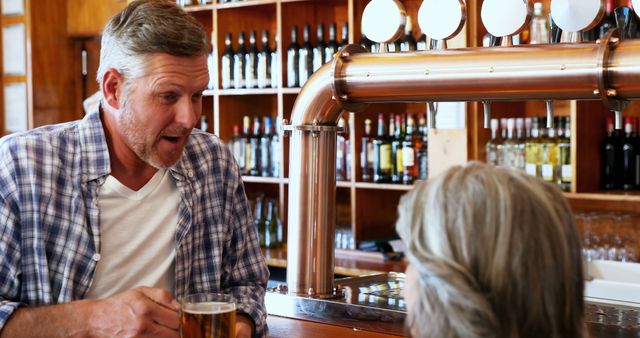 Man having a friendly conversation over a beer in a cozy pub bar. Perfect for use in articles or ads related to social gatherings, beer and alcohol marketing, bar and pub promotions, or lifestyle blogs highlighting social and leisure activities.