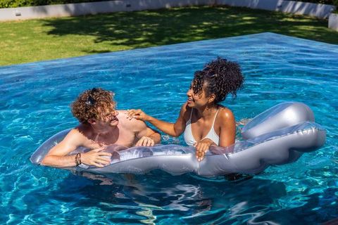 Couple lounging on inflatable float in backyard pool on sunny summer day