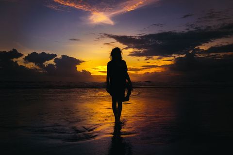 Silhouette of a Woman Walking on Shore at Sunset Beach
