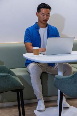 Young asian man working on laptop in cafe lounge with coffee cup, casual coworking