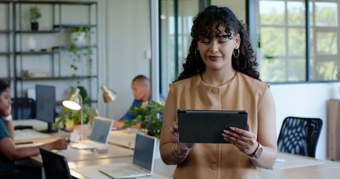 Woman in tan blouse using tablet leading diverse team in modern open-plan office