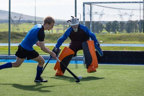 Field Hockey Player Dribbling Past Crouching Goalie on Turf