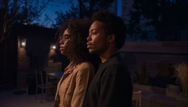 Twilight backyard couple standing side by side facing lantern-lit patio, contemplative mood