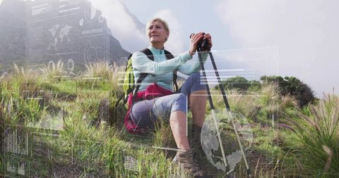 Mature woman sitting on grassy hillside holding trekking poles with AR tech overlay