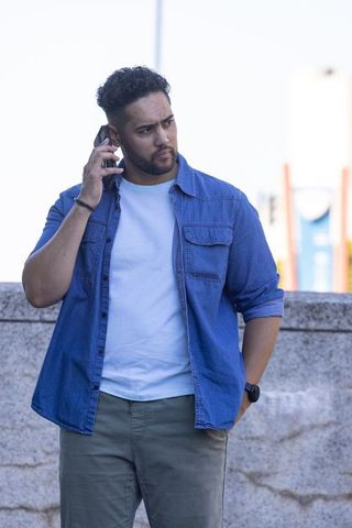 African american man talking on phone leaning on railing in denim shirt and wristwatch
