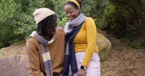 African American couple sharing cozy autumn moment smiling and leaning on rock in woodland