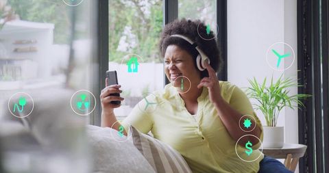 Woman enjoying music with headphones on couch using smartphone with ar icons for smart home