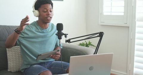 Young african american podcaster streaming and recording at home with microphone laptop