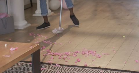 Man sweeping pink confetti from hardwood floor wearing casual.