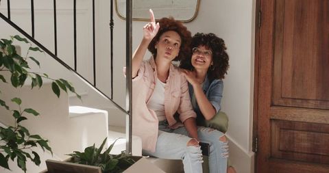 African American Friends Pointing Up on Stairs While Moving Into New Home, Smiling