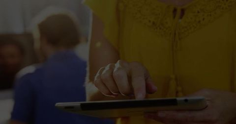 Woman holding tablet tapping touchscreen in cozy sunlit lounge wearing yellow top