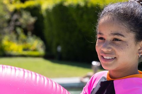 Smiling african american teen holding pink inflatable ring poolside wearing rash guard