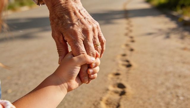 Holding hands across generations elder hand guiding child along sandy path with footprints