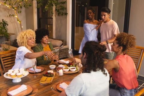 Diverse friends pouring wine and raising glasses laughing on outdoor patio dinner