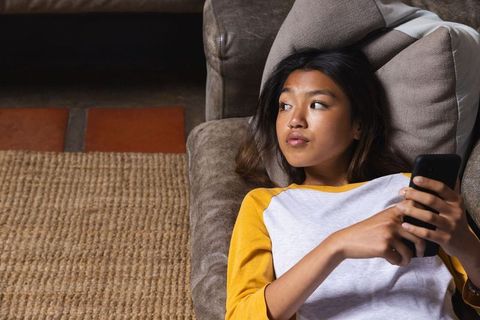 Teenage Asian Girl Relaxing on Sofa with Smartphone at Home