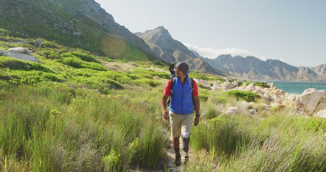 Middle-aged man hiking in lush, green mountain landscape under clear blue sky. Ideal for themes related to outdoor activities, adventure travel, fitness, healthy lifestyle, nature exploration, and environmental conservation.