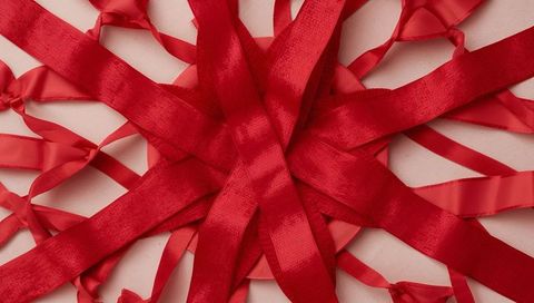Red satin ribbon starburst on pale surface with loose loops and textured strips