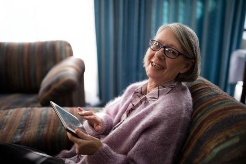 Senior woman relaxing on sofa using tablet for leisure