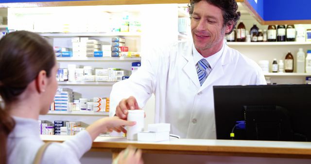 Pharmacist smiling while serving a customer in a well-stocked pharmacy, handing over medication. Use this for topics related to healthcare services, pharmacy operations, customer service in healthcare, and interactions between pharmacists and patients.
