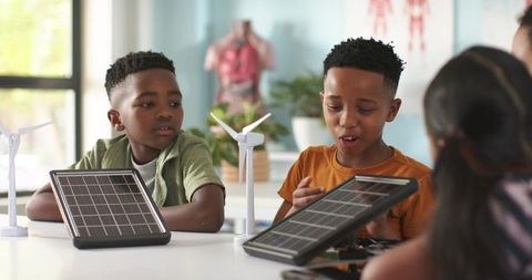 African american kids exploring solar panels and wind turbines in stem classroom