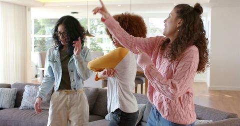 Laughing friends dancing and pointing in bright living room celebrating joyful friendship