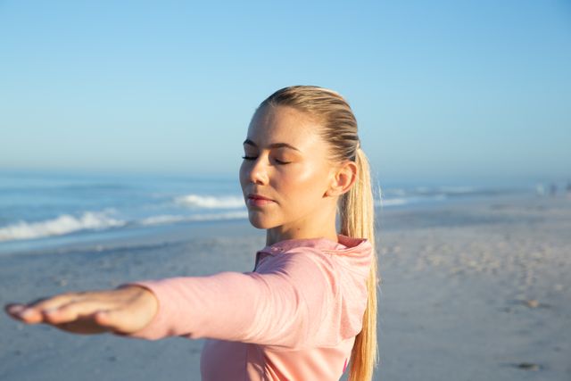 Caucasian woman wearing sports clothes, enjoying time at the beach on a sunny day, practicing yoga, arms stretched eyes closed.